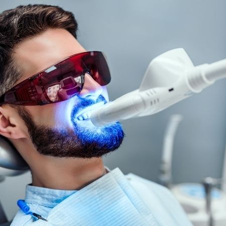 Mann mit Schutzbrille beim Zahnbleaching mit LED-Licht in einer modernen Zahnarztpraxis