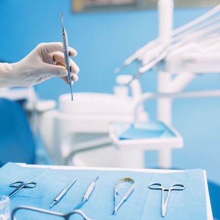 Zahnärztliche Instrumente auf einem blauen Steriltuch, im Vordergrund eine behandschuhte Hand mit einem Werkzeug