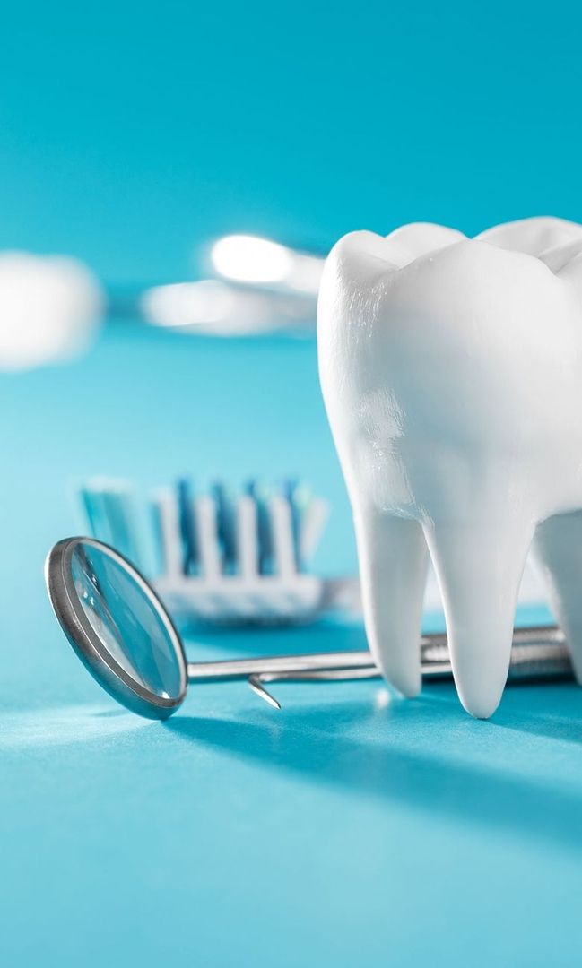 Modell eines Zahns mit Zahnarztspiegel und Zahnbürste im Hintergrund auf blauem Untergrund