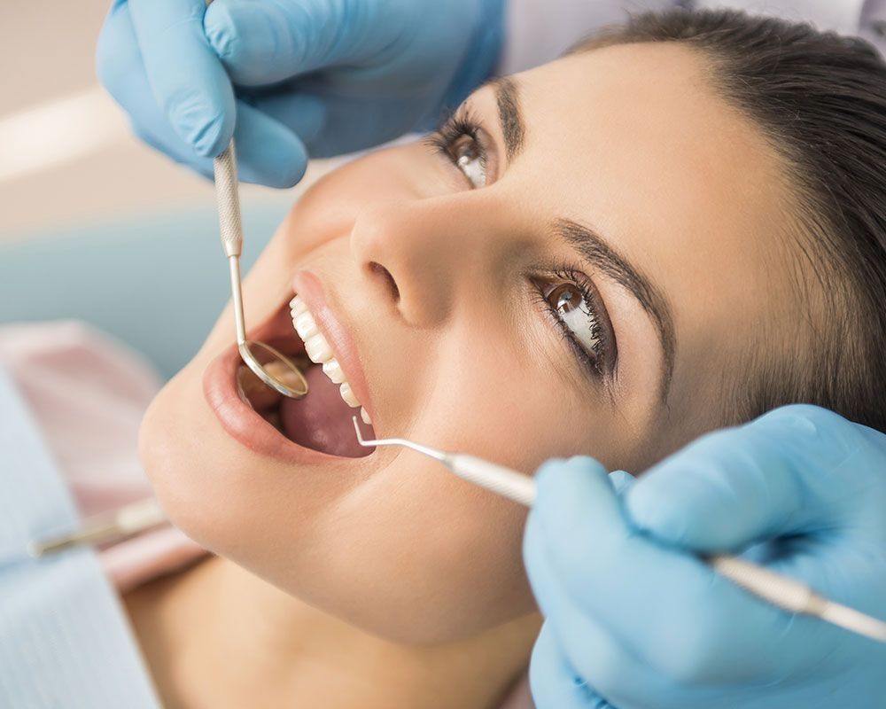 Junge Frau bei zahnärztlicher Untersuchung mit geöffnetem Mund und Spiegel