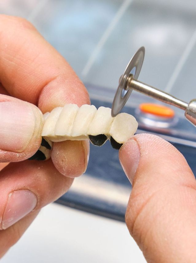 Zahntechniker schleift Zahnbrücke mit rotierender Trennscheibe