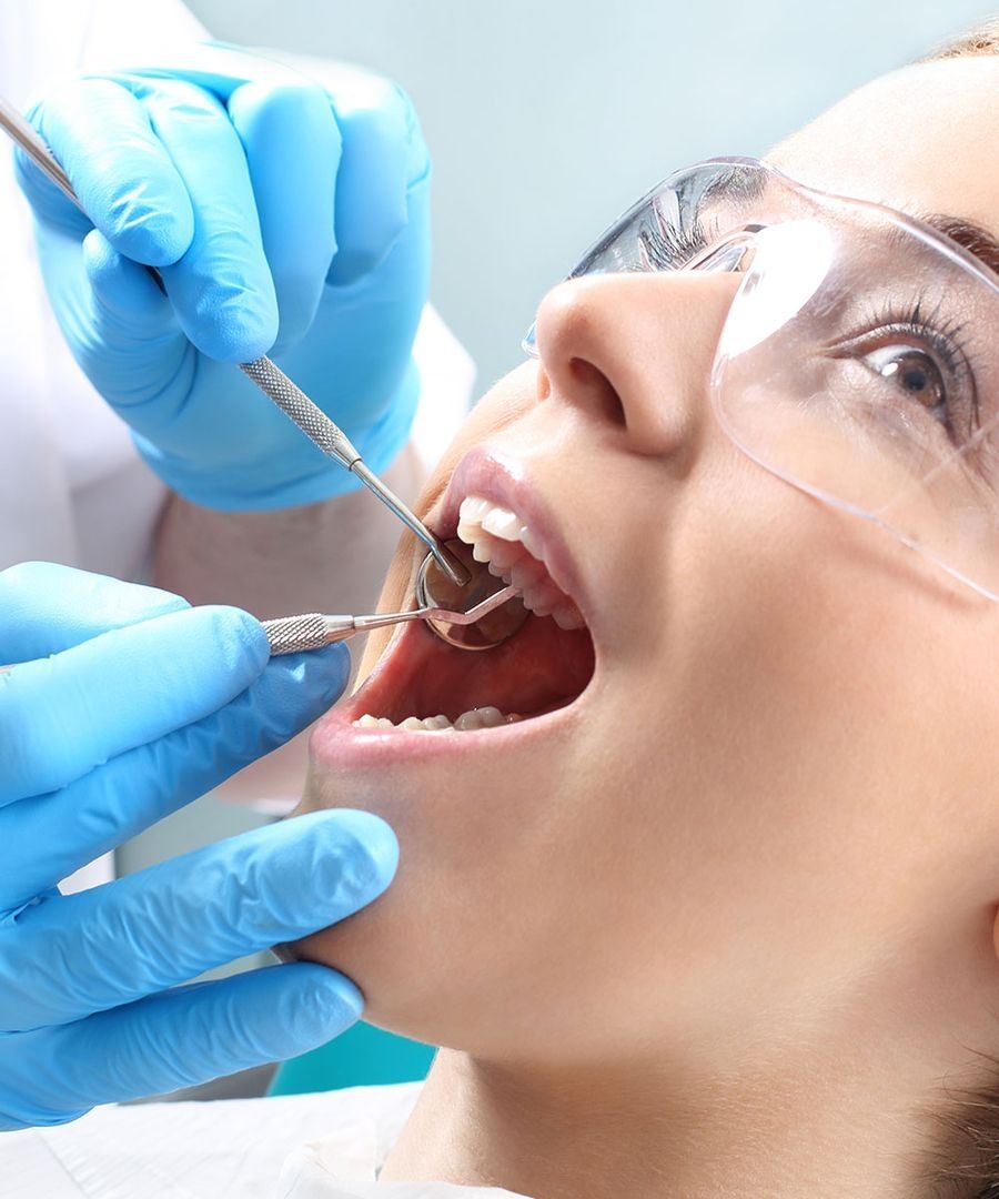 Zahnärztliche Behandlung bei einer Patientin mit Schutzbrille und geöffnetem Mund