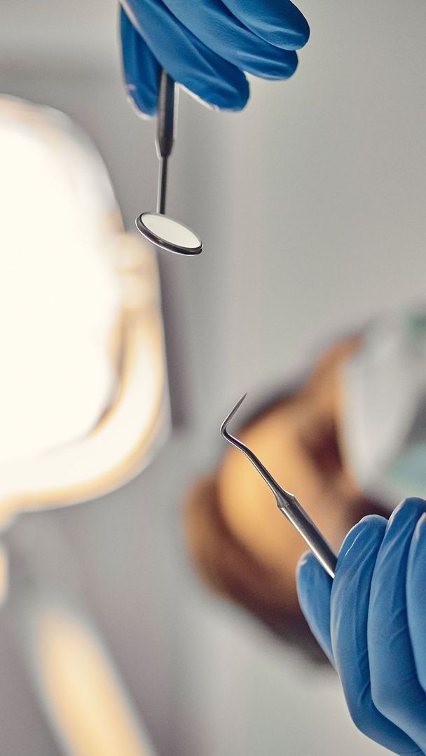 Blick aus der Perspektive des Patienten auf zwei zahnärztliche Instrumente in behandschuhten Händen
