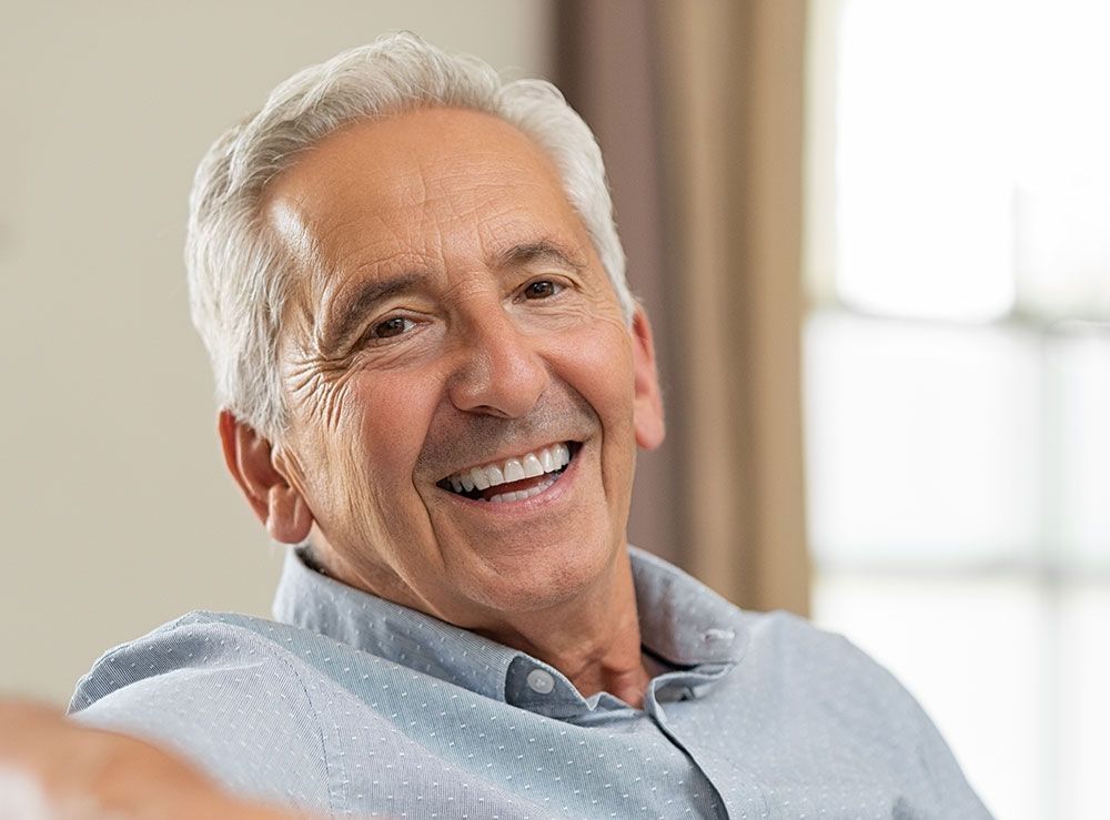 Älterer Mann mit grauen Haaren lächelt zufrieden und zeigt seine Zähne